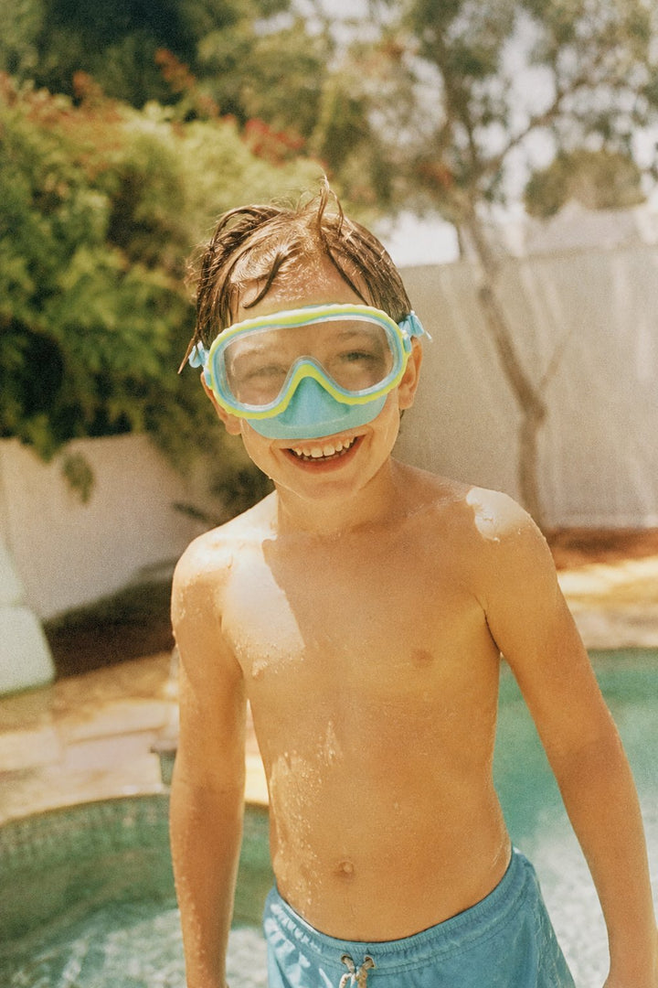 Child smiling in a Citrus Aqua Lakeday swim mask by the pool