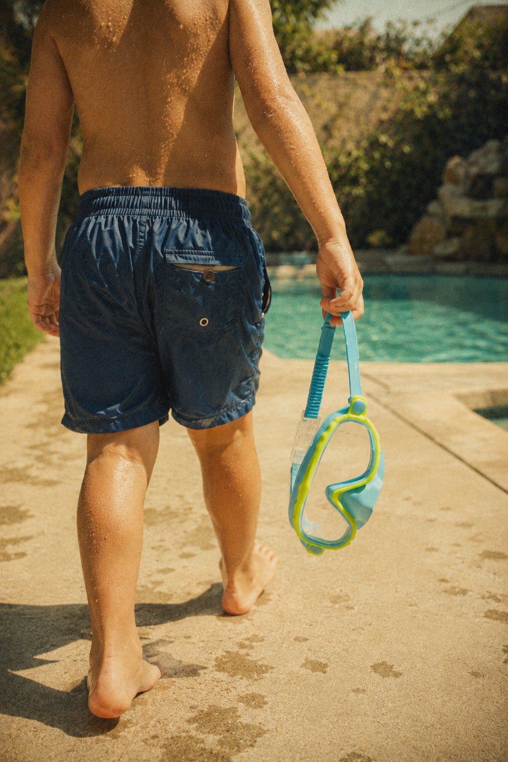 Child carrying Lakeday goggles toward a backyard pool